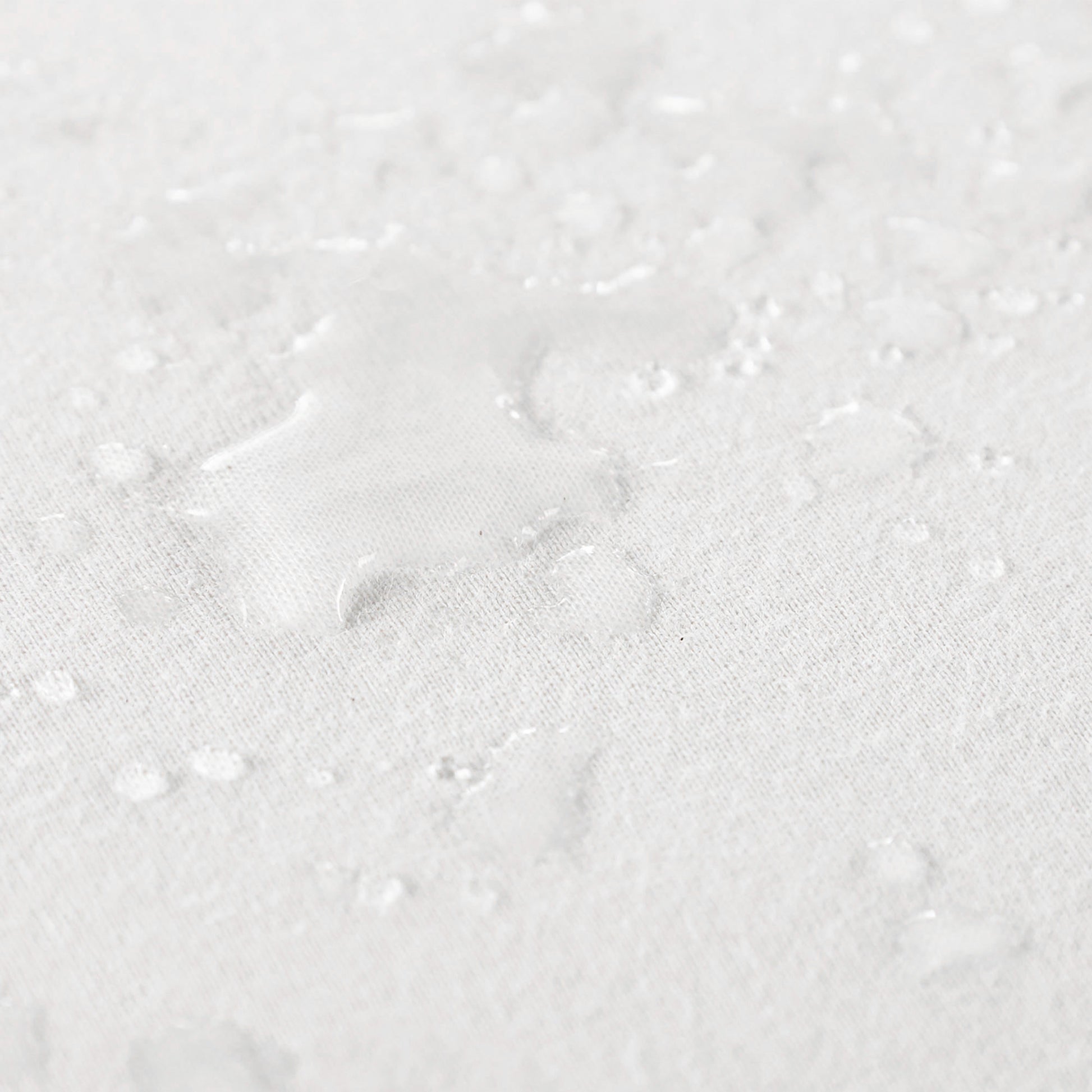 Close up view of water spilled on organic cotton waterproof pique knit crib mattress pad, showing its liquid-repelling surface