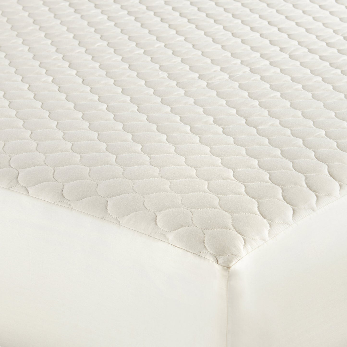 Ivory organic cotton mattress pad on bed with soft diamond quilting.