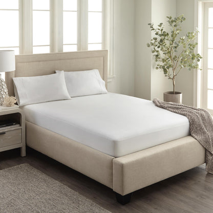 Fitted white organic waterproof pique mattress cover shown on a bed in a beautifully lit bedroom setting.