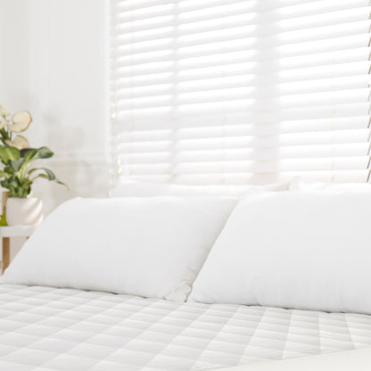 Luxury organic mattress pad on bed with white pillows, sunlight filtering through shaded window behind