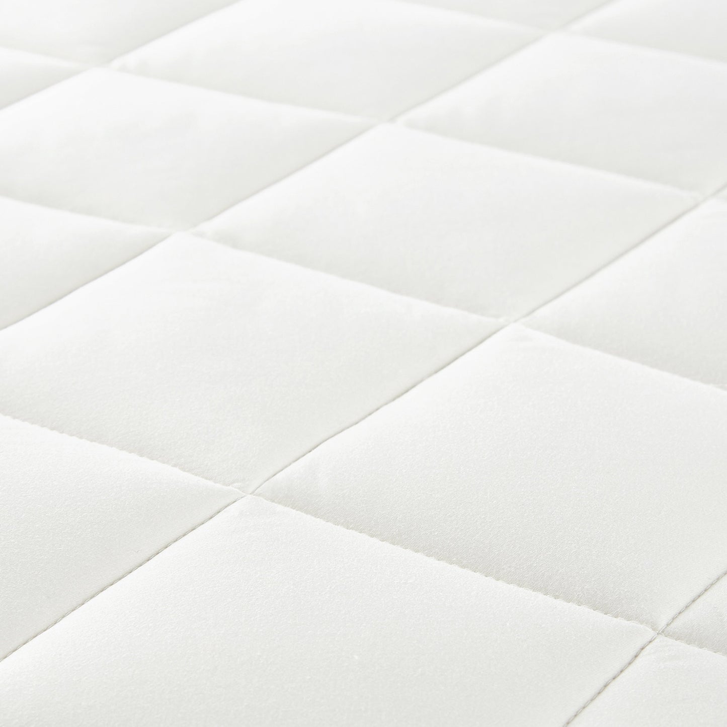 Angled view of white luxury organic mattress protector on bed with soft square stitching.