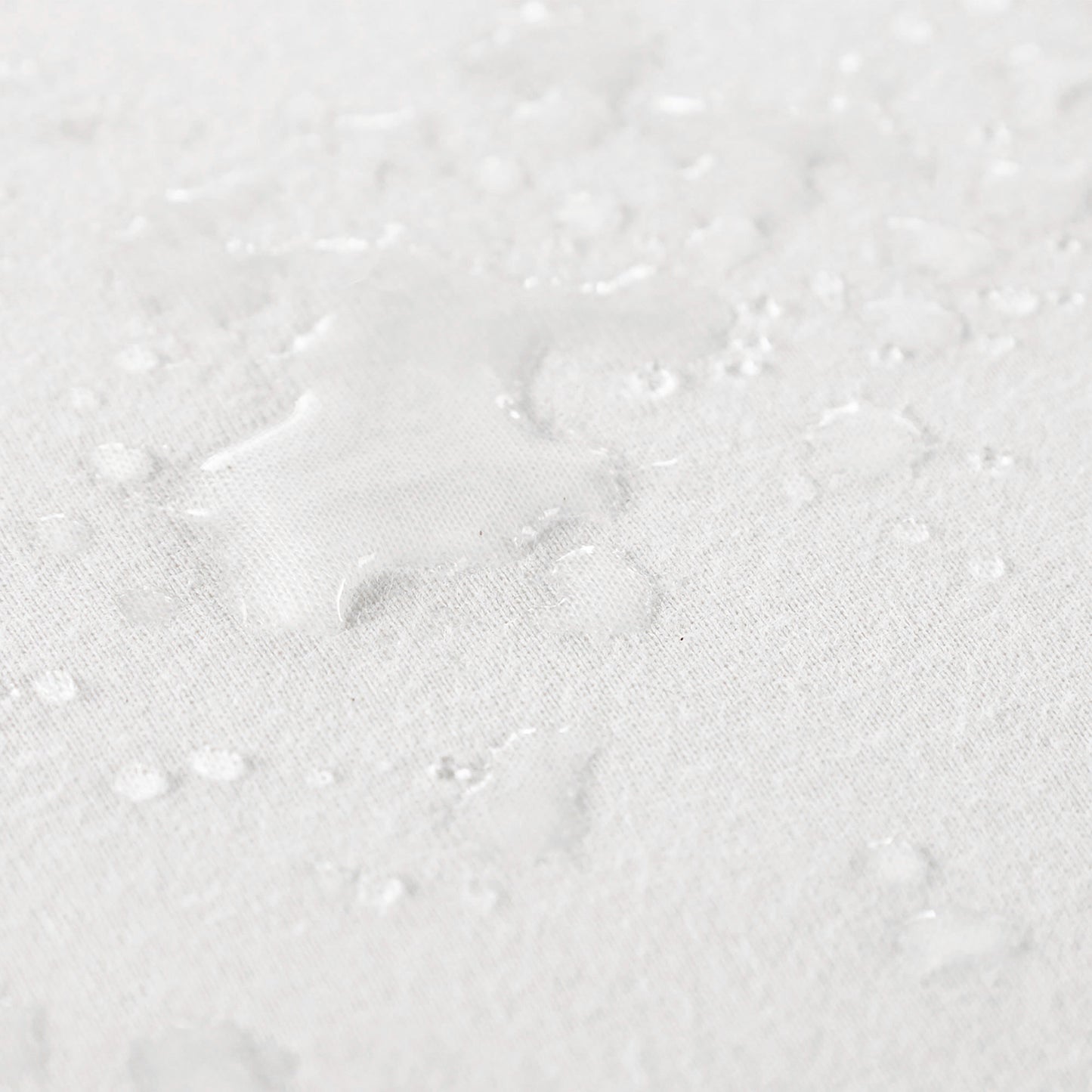 Close up view of water spilled on organic cotton waterproof pique knit crib mattress pad, showing its liquid-repelling surface