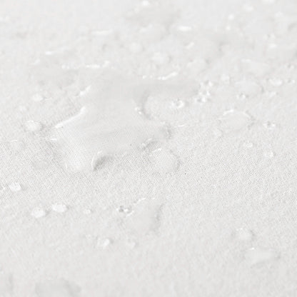 Close up view of water spilled on organic cotton waterproof pique knit crib mattress pad, showing its liquid-repelling surface