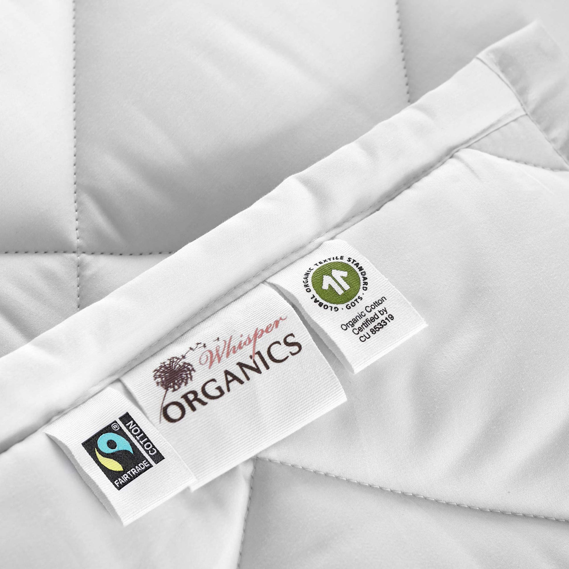 Close-up of a organic cotton comforter with fairtrade and GOTS certification labels next to 'Whisper Organics' label.