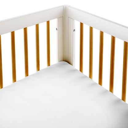 Close-up of white waterproof organic cotton jersey knit crib mattress protector tucked tightly into wooden crib corner