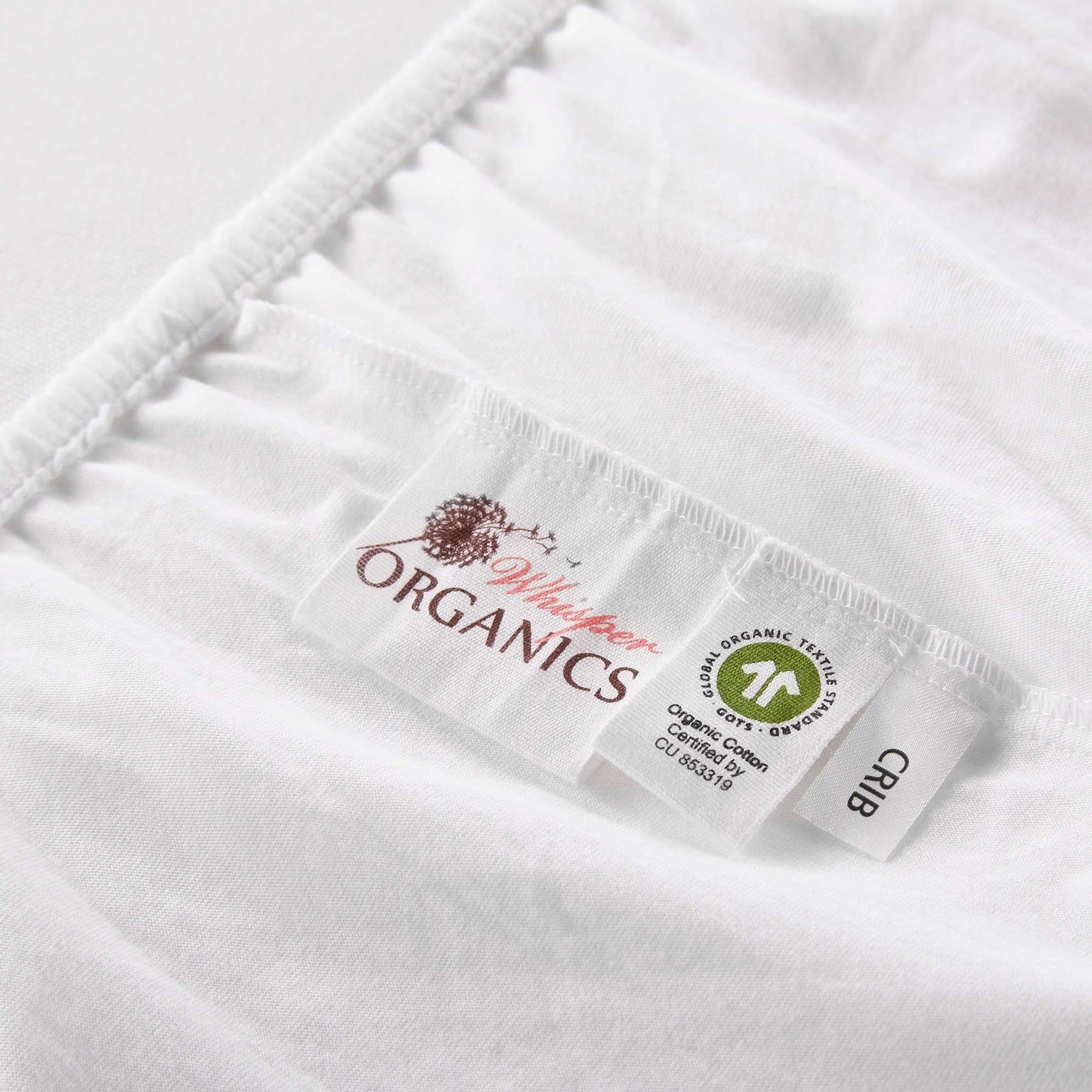 Zoomed in view of tags on mattress pad showing GOTS certification alongside Whisper Organics logo and crib tag.
