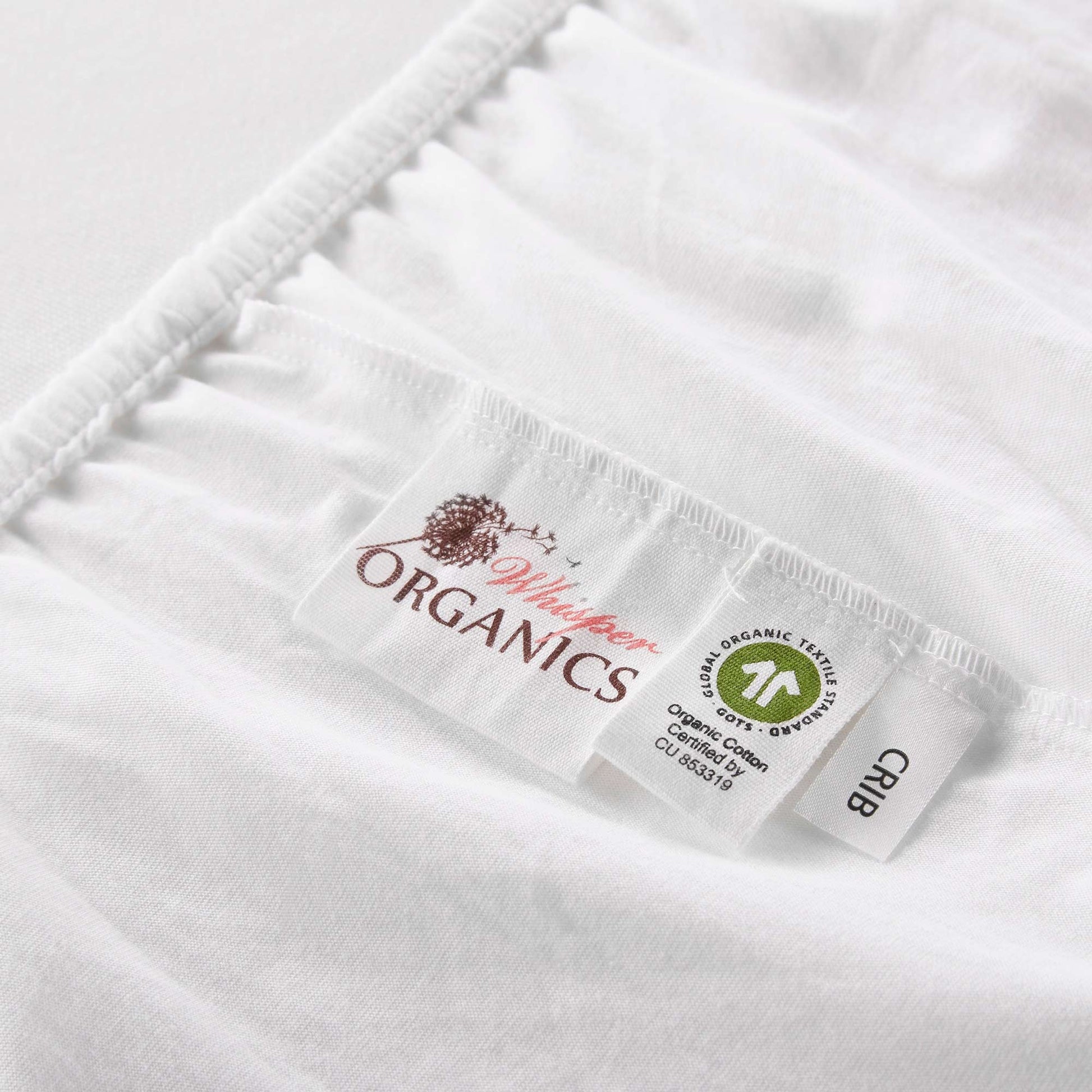 Zoomed in view of tags on mattress pad showing GOTS certification alongside Whisper Organics logo and crib tag.