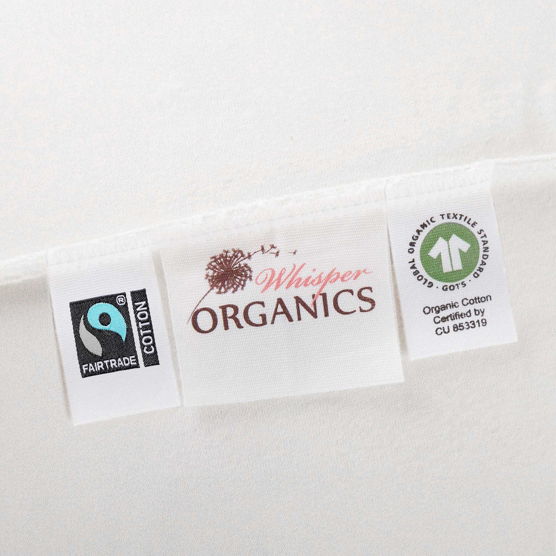 Close-up of tags on mattress pad showing Fairtrade and GOTS certification alongside Whisper Organics logo