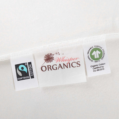 Close-up of tags on mattress pad showing Fairtrade and GOTS certification alongside Whisper Organics logo