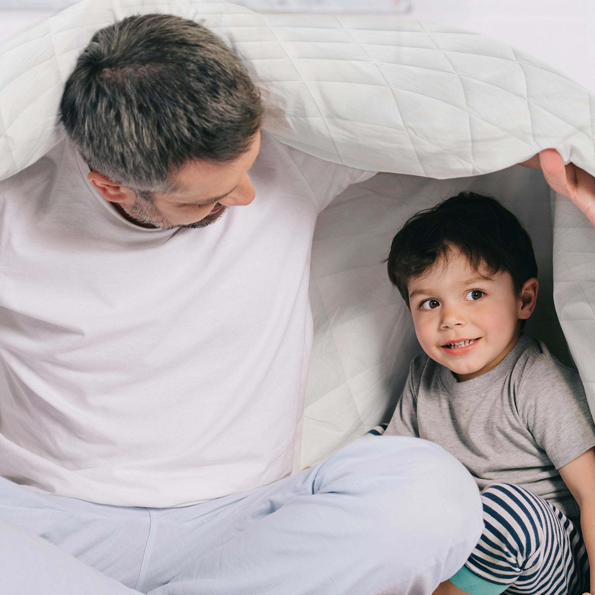 Man and child playing under white organic cotton comforter