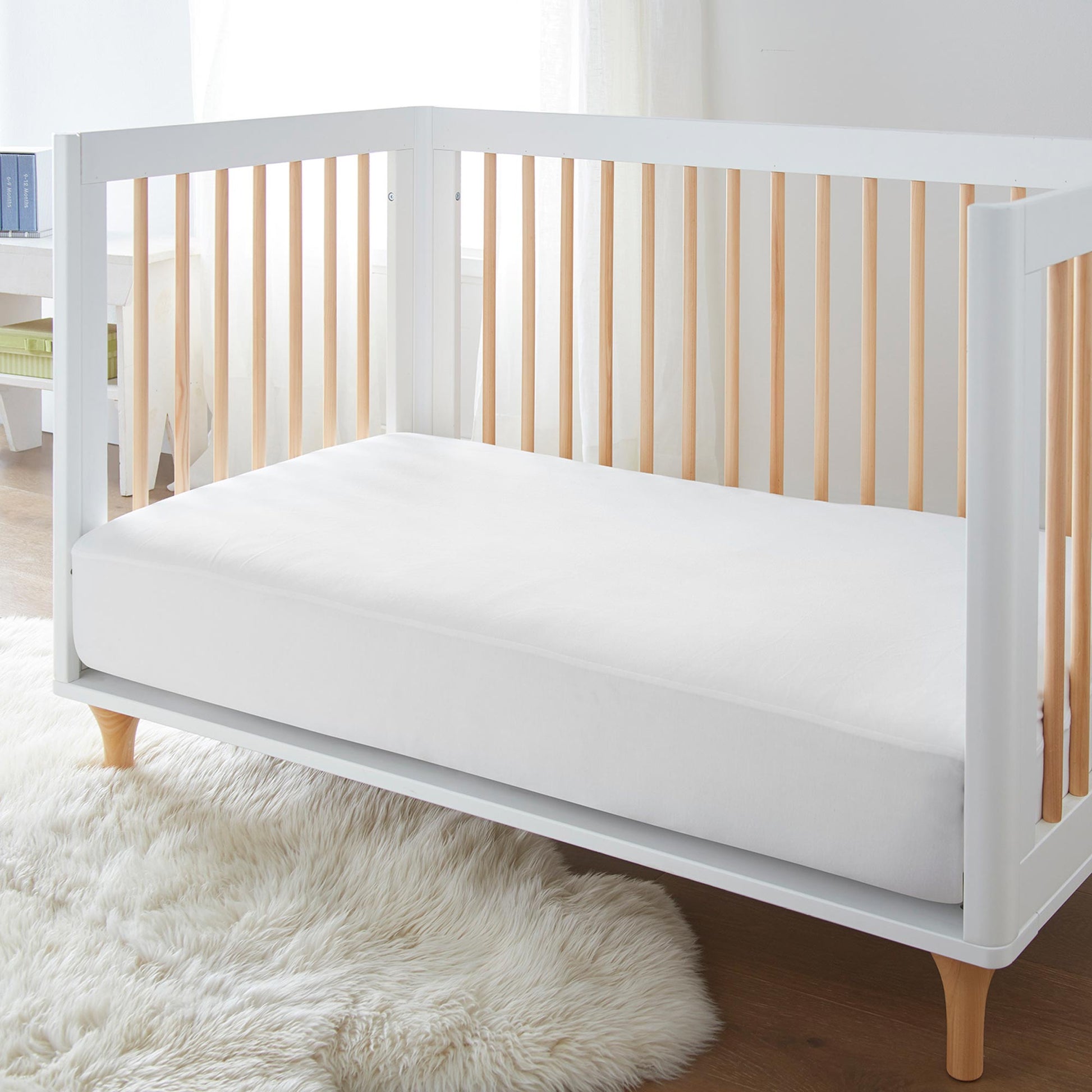 White waterproof organic cotton jersey knit crib mattress pad on modern wooden crib with rug underneath